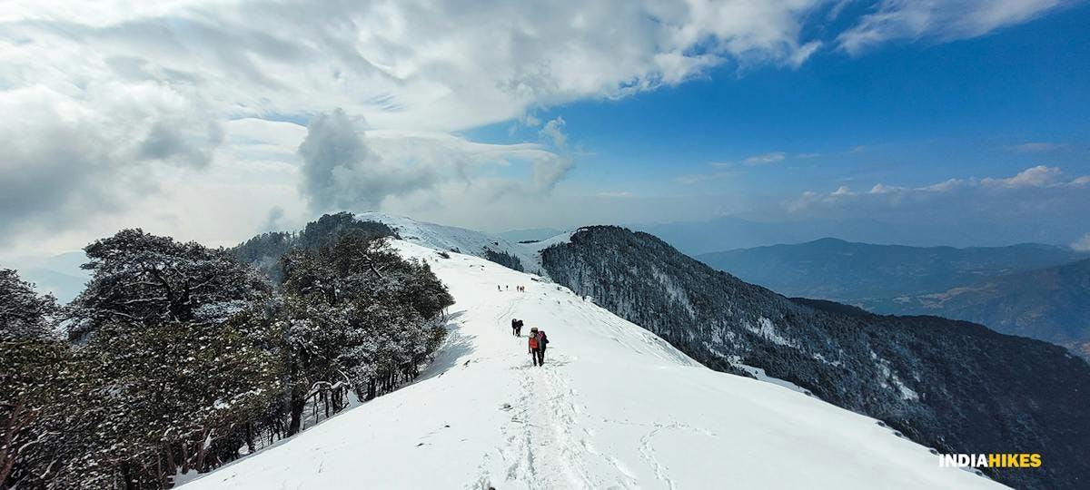 A group of trekkers traversing through ankle deep snow on a ridge in the months of February and Early March