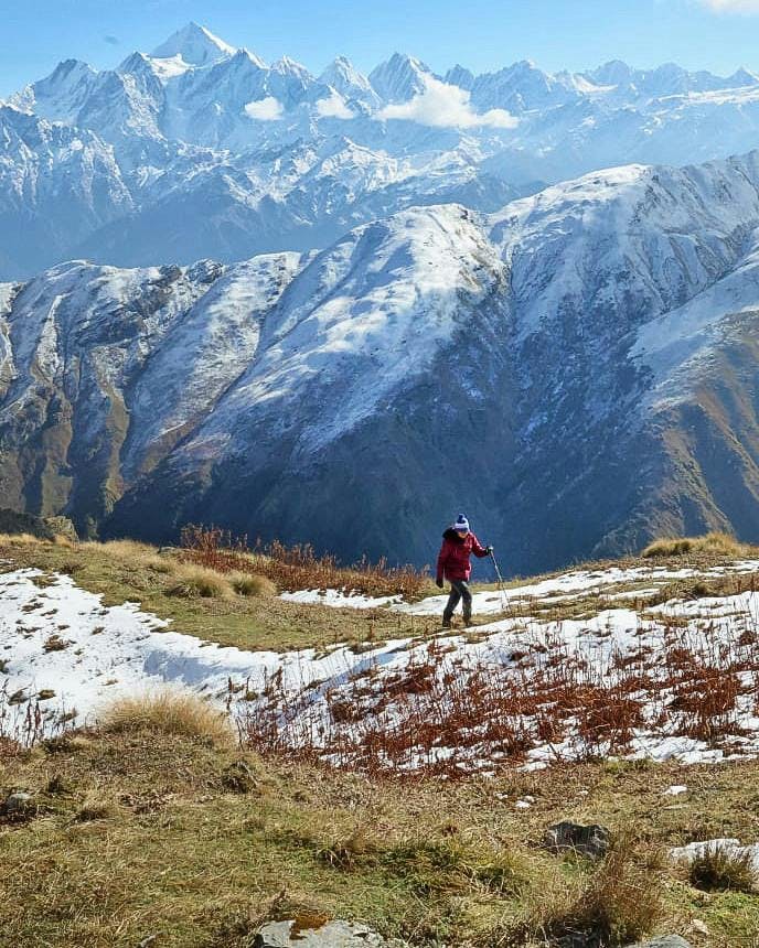 A trekker walking with snow capped-mountains in the background at the Ranthan Top trek